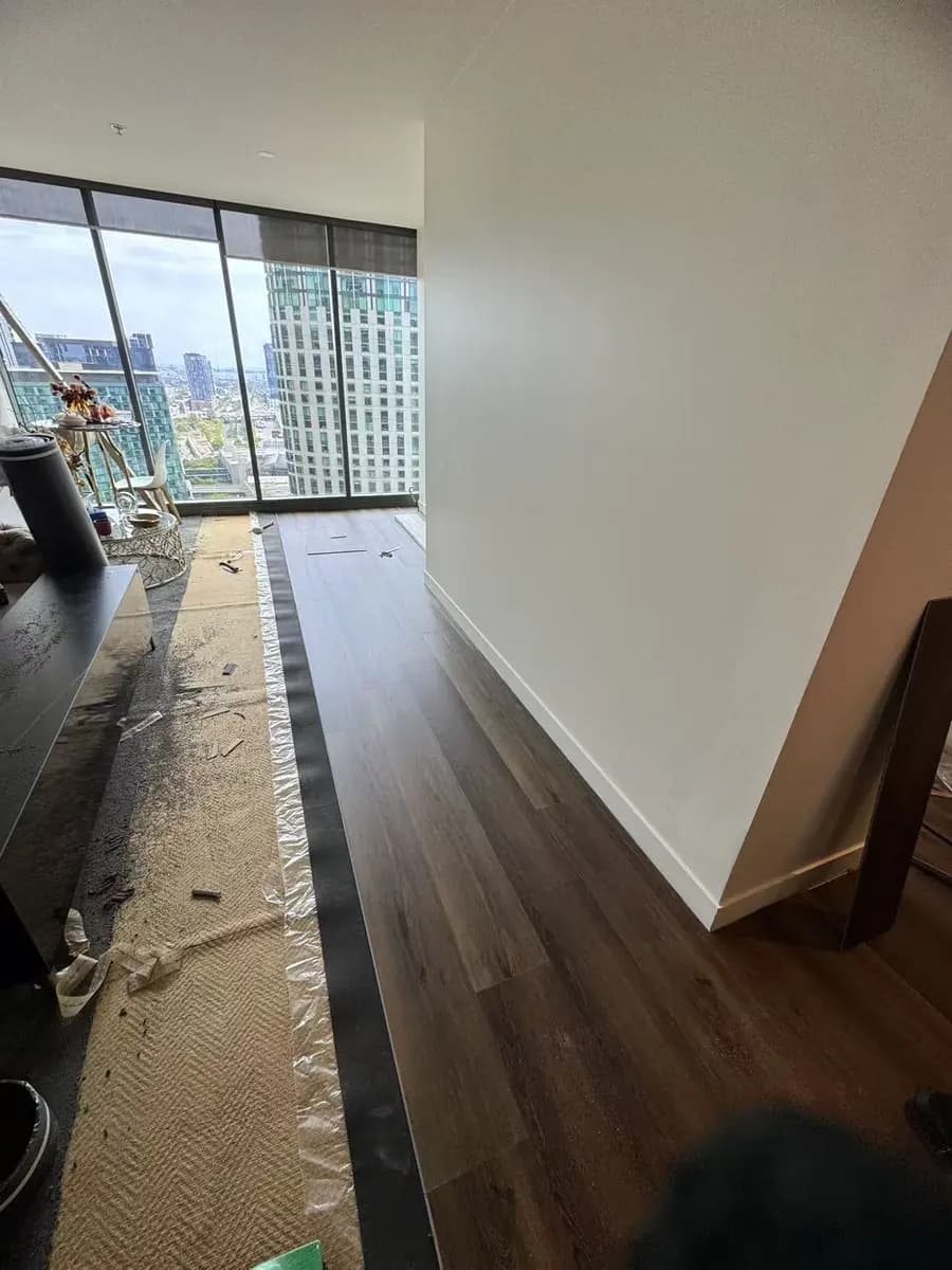 Dark plank flooring being installed beside a protected work area in a high-rise living room