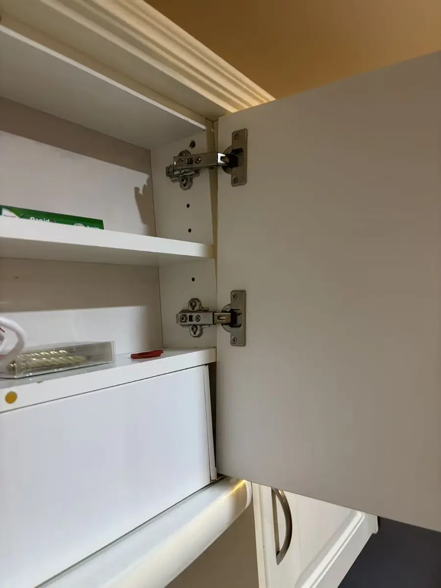 Close-up of concealed hinges inside a white kitchen cabinet before realignment