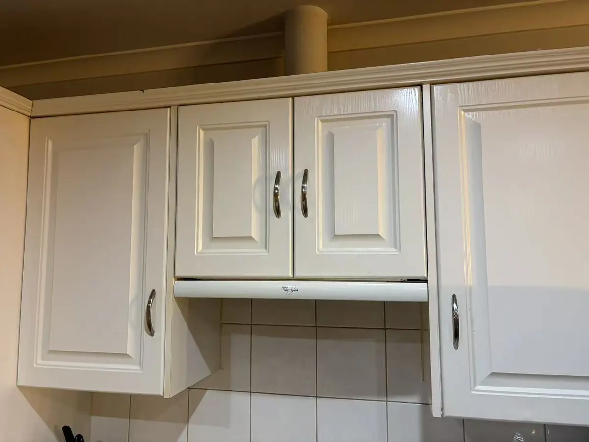 White raised-panel kitchen cabinet doors aligned above the rangehood after repair