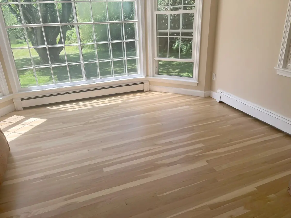 Sunlit empty room with light wood flooring and large multi-pane windows