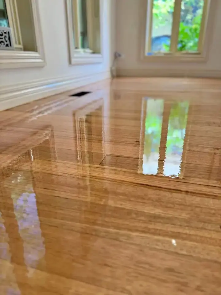 Close-up of a glossy timber floor reflecting windows and wall trim