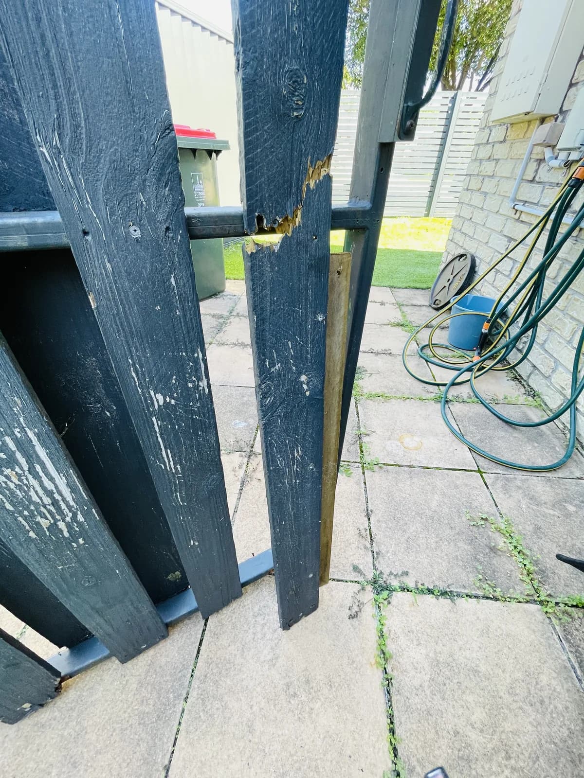 Split and missing timber beside the latch-side frame of a dark painted gate