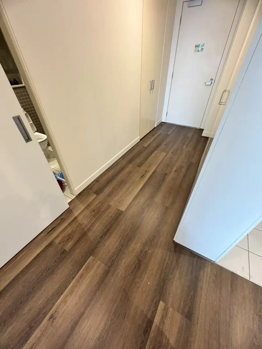Dark plank flooring running through an apartment hallway with white storage doors