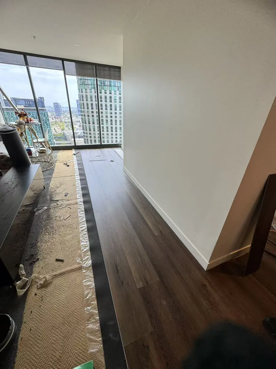 Dark plank flooring being installed beside a protected work area in a high-rise living room