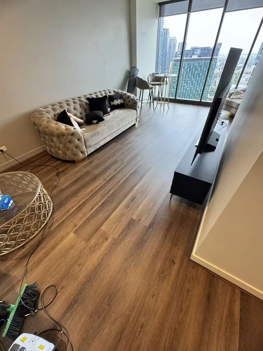 Dark plank flooring across a furnished high-rise living room with installation tools visible