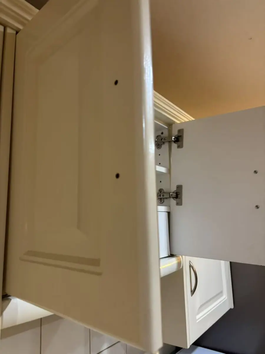 Open kitchen cabinet door showing the hinge area before adjustment