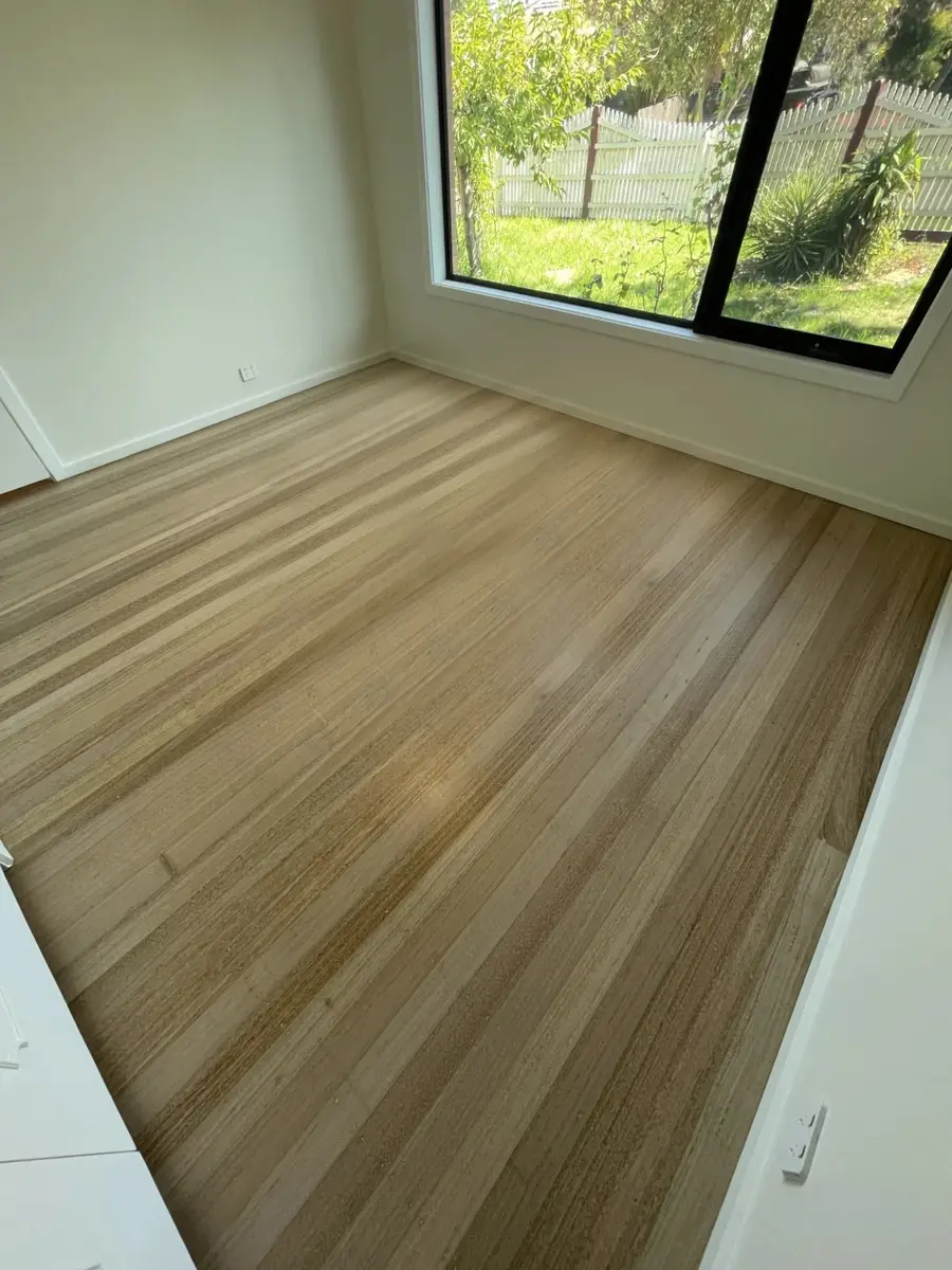 Light-toned timber flooring in a bright empty room beside a black-framed window